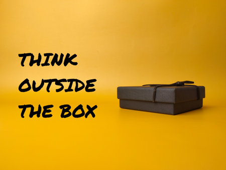 Black box with the word THINK OUTSIDE THE BOX on yellow backgroundの写真素材