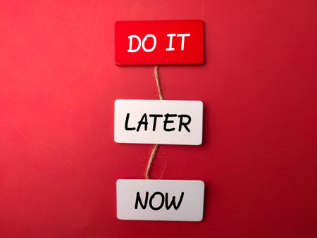 Colored wooden board with the word DO IT LATER NOW on a red backgroundの写真素材