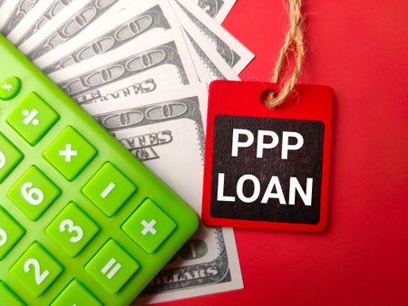 Banknote,calculator and wooden board with the word PPP LOAN on a red backgroundの写真素材