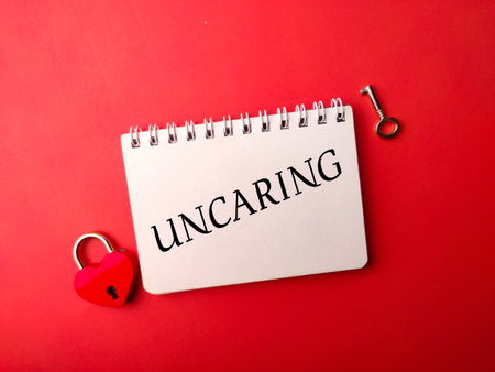 Notebook and love padlock with the word UNCARING on a red backgroundの写真素材