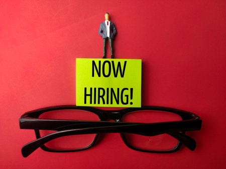Glasses and miniature people with the word NOW HIRING on a red backgroundの写真素材