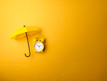 Top view yellow umbrella and yellow alarm clock on a yellow background with copy spaceの写真素材