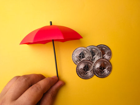 Someone hand holding red umbrella covered bitcoins on a yellow backgroundの写真素材