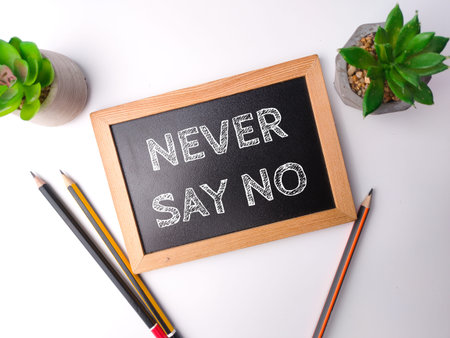 Wooden black board and pencil with the word NEVER SAY NO on white background