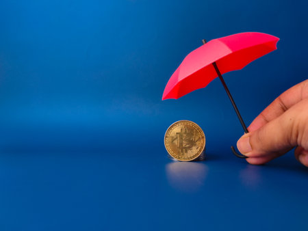 Someone hand holding red umbrella covered bitcoins umbrella covered bitcoins on a blue backgroundの写真素材
