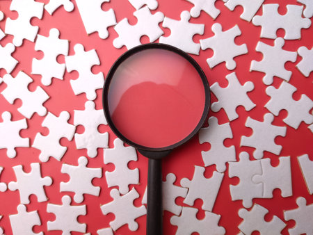 Top view white puzzle and magnifying glass on a red background.の写真素材