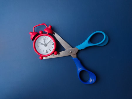 Closeup blue scissors with red alarm clock on a blue backgroundの写真素材
