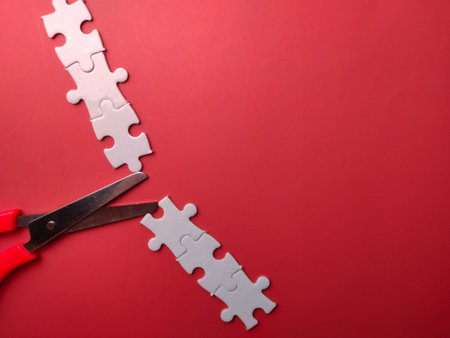 Closeup red scissors cutting white puzzle on a red background with copy spaceの写真素材