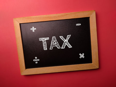 Black wooden board with the word TAX on a red backgroundの写真素材