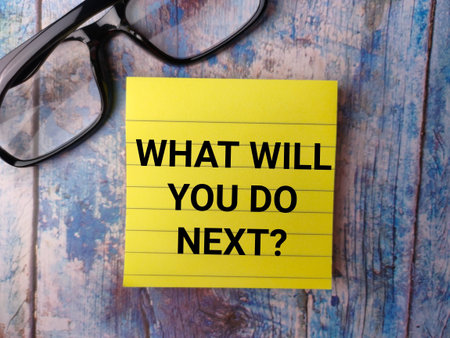 Glasses and sticky note with the word WHAT WILL YOU DO NEXT on a wooden background