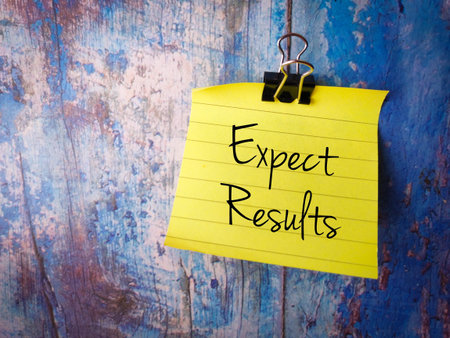 Paper clip and sticky note with the word Expect Result on a wooden background