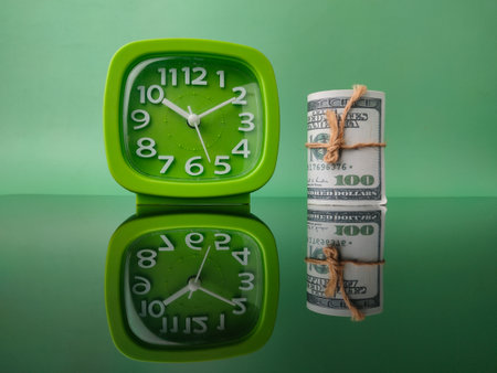 Banknotes and green clock on green background with reflection on a black acrylic boardの写真素材