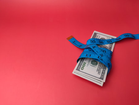 Measuring tape wrapped around dollar bills on a red background with copy space.の写真素材