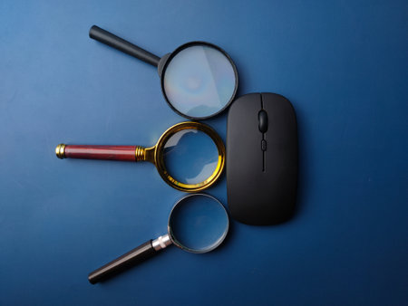 Top view magnifying glass and wireless mouse on a blue backgroundの写真素材