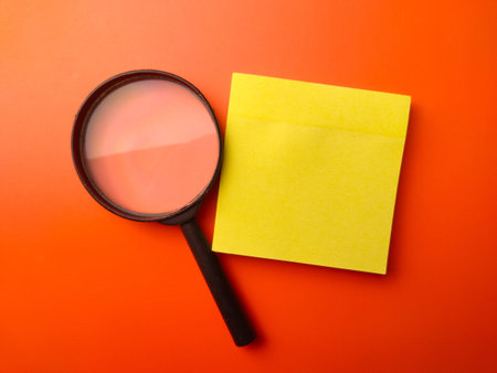 Top view sticky note and magnifying glass on a orange background with copy and text space.