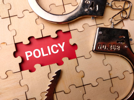 Wooden puzzle and handcuff with written word POLICY on a red background.の写真素材