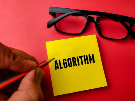 Hand holding pencil and sticky note with text ALGORITHM on red background.の写真素材