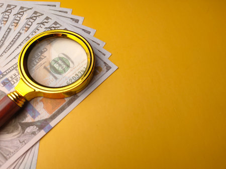 Closeup gold magnifying glass and one hundred dollars on a yellow background.の写真素材