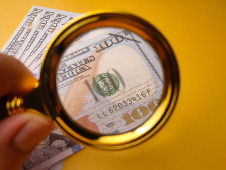 Closeup gold magnifying glass and one hundred dollars on a yellow background.