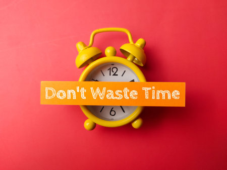 Alarm clock and sticky note with the word Dont waste time on red background.