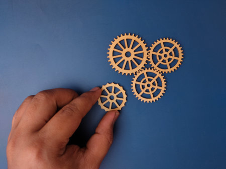 The image shows a hand holding a small wooden gear, with three other similar gears arranged on a blue background.の写真素材