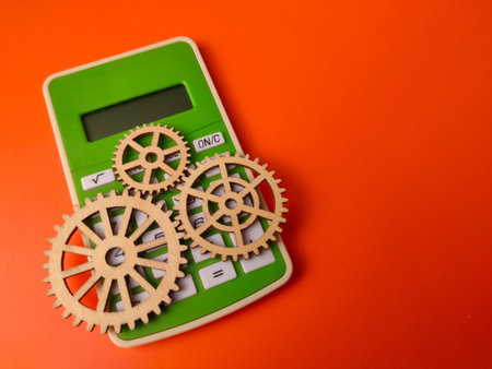 Closeup green calculator accompanied by three wooden gears on an orange background.
