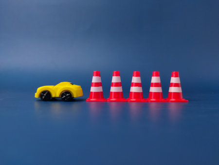 This image shows a small yellow toy car surrounded by four miniature traffic cones on a blue background.の写真素材