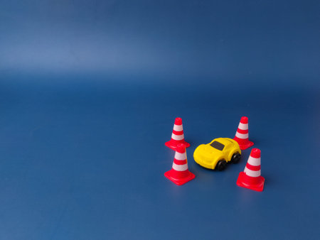 This image shows a small yellow toy car surrounded by four miniature traffic cones on a blue...