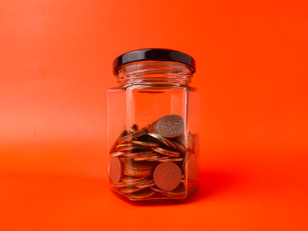 The image shows a glass jar filled with coins, which is a common representation of saving money.の写真素材
