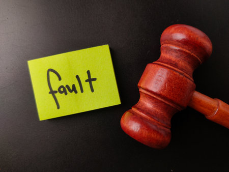 The image shows a wooden gavel next to a yellow sticky note with the word fault written on it.の写真素材