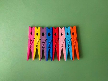 The image shows a row of colorful wooden clothespins on a green background.の写真素材