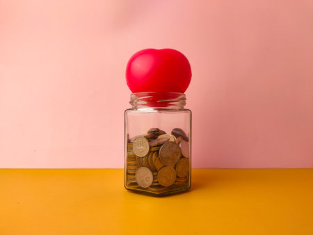 A red, heart-shaped object on top of the jar could symbolize saving for personal goals.の写真素材
