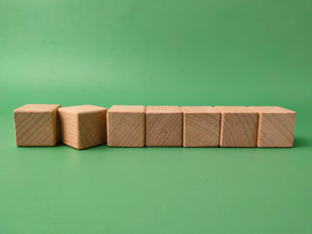 The image displays seven natural, unfinished wooden cubes arranged in a line on a green background.の写真素材