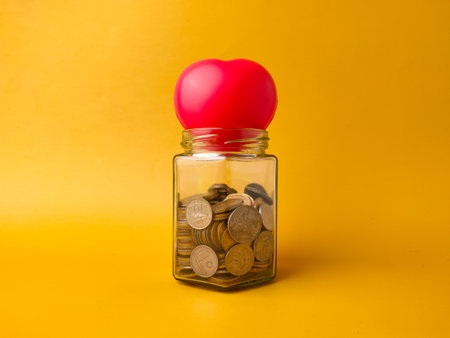 A red, heart-shaped object on top of the jar could symbolize saving for health, love, or personal goals.の写真素材