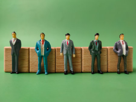 The image displays five miniature figures of businessmen standing behind small wooden blocks.の写真素材