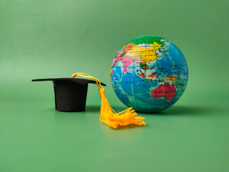 Miniature graduation cap and a small globe against a green background.の写真素材