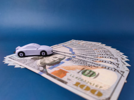 The image displays a toy car on a pile of US one-hundred-dollar bills, representing concepts such as car insurance, saving money, or purchasing a vehicle.の写真素材