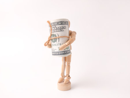 This image depicts a small wooden artist's mannequin holding a roll of hundred-dollar bills.の写真素材