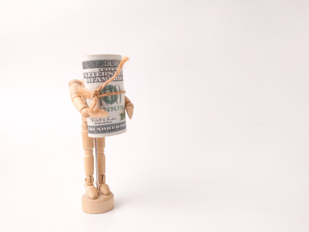 This image depicts a small wooden artist's mannequin holding a roll of US hundred-dollar bills.の写真素材