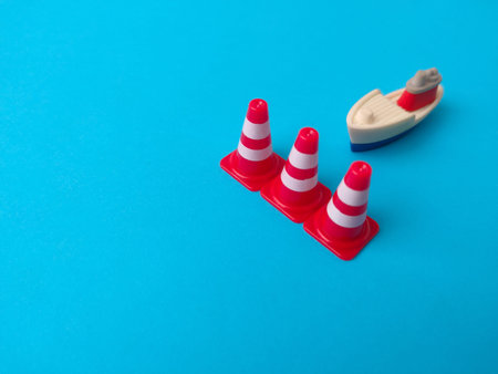 Miniature plastic traffic cones and a toy boat on a blue background.