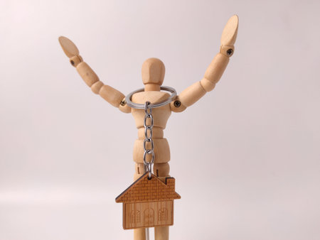 Wooden house-shaped keychain, held by an artist's wooden mannequin.