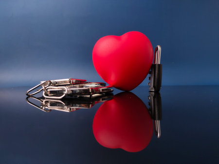 Red, heart-shaped object next to a small black padlock and a set of keys, symbolizing love and...