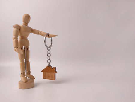 Wooden house-shaped keychain, held by an artist's wooden mannequin.の写真素材