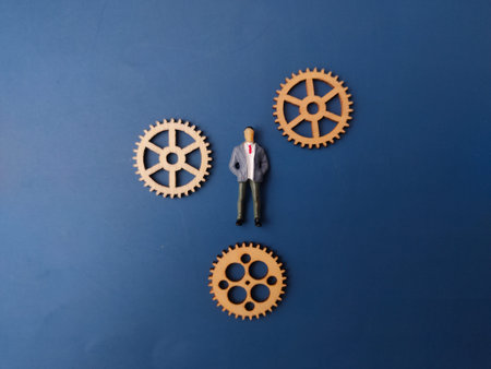 Miniature figurine of a businessman positioned among several wooden gears.の写真素材