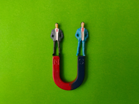 The image shows two miniature figures of people in suits standing on a magnet on a green background.