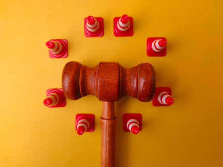 Wooden gavel positioned in the center of several miniature traffic cones on a yellow surface.