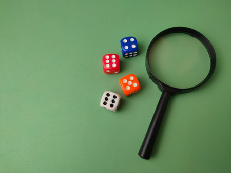 A high-angle, conceptual still life featuring a black magnifying glass and four colorful dice on a...