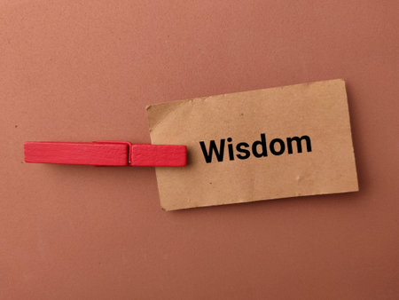 high-angle conceptual shot on a warm brown background featuring a small piece of brown kraft paper with the word Wisdom.