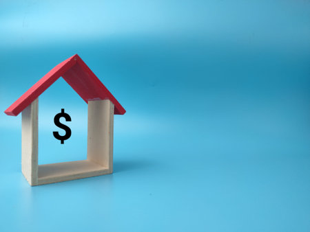 A miniature wooden house model with a red roof displays a black dollar sign inside, set against blue.