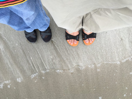 Selfie of couple feet at the beach. Top view of human feet standing on the sand at beach. Love and...